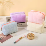Four colorful quilted makeup bags on a light surface with a brush and compact mirror.