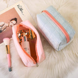 Pink makeup pouch with cosmetic items and a gray pouch on a fluffy surface