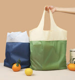 Two color-blocked tote bags, one blue and white, one green and beige, on a beige background with fruits.