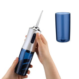Hand holding a blue and silver dental water flosser with a blue cup on a white background
