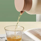 Tea being poured from a pink teapot into a glass on a light surface with a green background