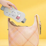 Hand holding a gray device with a cartoon character on a pink textured bag against a yellow background