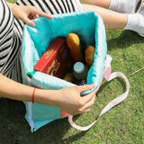 Turquoise and pink quilted 2-in-1 picnic mat bag unfolded on grass with picnic snacks_ corporate gift_customised gift singapore