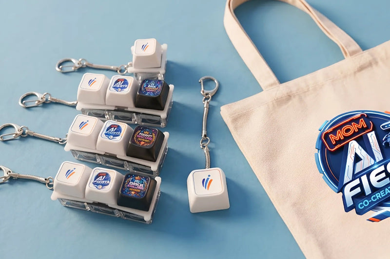 A set of AI keycap keychains with clear plastic cases, silver keyrings, and white keycaps featuring colorful graphics, displayed next to a beige canvas tote bag with a 'MOM AI FIEF CO-CREATE' logo on a light blue background.