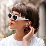 Person wearing white sunglasses and wireless earbuds with a blurred outdoor background