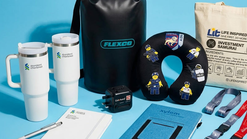 Collection of promotional items including tumblers, a backpack, and a neck pillow on a blue background.