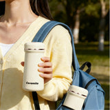 Person holding a white ceramic mug with 'Ceramito' branding, wearing a yellow sweater and blue backpack outdoors.