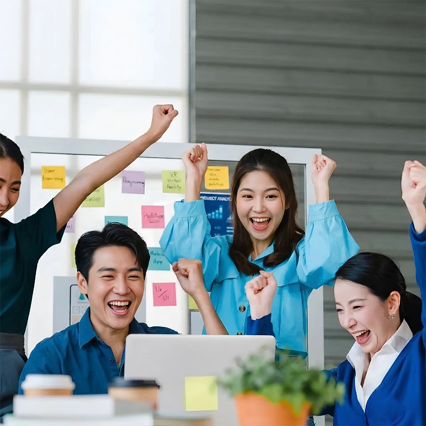 Group of happy employees in an office with raised fists, celebrating.