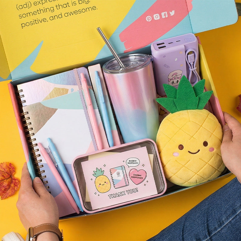 Assorted stationery items including a plush pineapple, notebooks, and a tumbler on a yellow background.