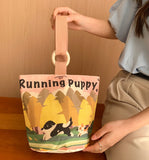 Person holding a small bag with 'Running Puppy' design against a wooden background