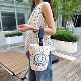 Person holding a white tote bag with blue handle and smiley face design .