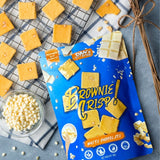 Blue package of Dan's Brownie Crisp White Chocolate on a gray surface with crackers and white chocolate chips.