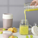 Person pouring a green smoothie from a Thermos container into a glass jar on a table with fruits.