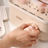 Hand adjusting a knob on a Thermos food container with kitchen utensils in the background.