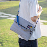Person holding a gray and blue bag outdoors on a grassy field
