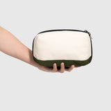 Hand holding a green and white rectangular pouch against a light gray background