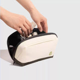 Person placing items into a white toiletry bag with a visible brand logo on a light gray background