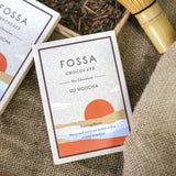 FOSSA Chocolate Uji Hojicha packaging on a textured surface with tea leaves and a bamboo whisk.