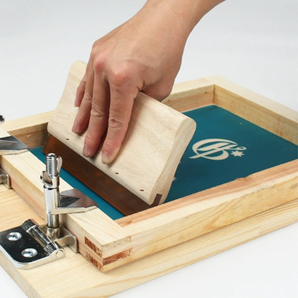 Hand using a wooden stamping tool on a green surface with a visible brand logo.