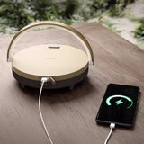 Round beige device with a cable connected to a smartphone on a wooden surface.