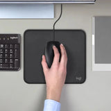 Logitech B100 corded USB mouse being used on a gray felt desk mat next to a laptop, a reliable tech essential for corporate gifting._customised corporate gift singapore