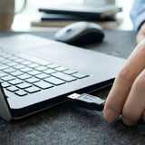 Close-up of a user connecting the USB-A cable of a Logitech B100 mouse into a laptop, highlighting its plug-and-play setup._customised corporate gift singapore
