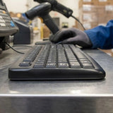 Side-angle view of the rugged, spill-resistant Logitech K120 keyboard being used at an industrial workstation, highlighting its durability for heavy-duty corporate use._Customised Corporate Gift