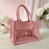 Natural jute tote bag with a clear PVC display window and padded handles on a grassy background_corporate jute bag_corporate door gift