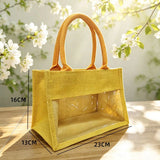 Natural jute tote bag with a clear PVC display window and padded handles on a grassy background_corporate jute bag_corporate door gift