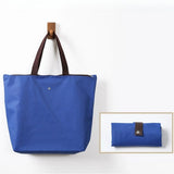 Vibrant deep blue Premium Foldable Oxford Waterproof Tote Bag hanging on a wooden hook with folded color options_ customised corporate gift singapore