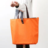 Vibrant orange Premium Foldable Oxford Waterproof Tote Bag hanging on a wooden hook with folded color options_ customised corporate gift singapore