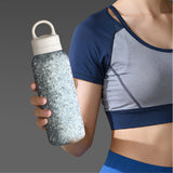 Person holding a textured water bottle with a gray and white design, wearing a sports outfit.