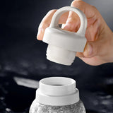 Hand holding a white silicone lid over a gray water bottle
