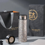 Premium Titanium Thermos Bottle with black lid on a gray surface next to a black bag