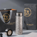 Premium Titanium Thermos Bottle with black lid on a gray surface next to a black bag