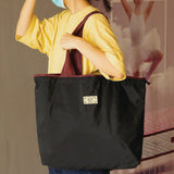 Person holding a black tote bag with a visible brand label against a neutral background