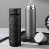 Two black Titanium Hygienic Thermal Bottle on a gray surface with a digital clock in the background.