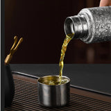 Silver bottle pouring liquid into a small metal cup