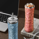 Two glittery tumblers, one blue and one pink, on a desk next to a laptop.
